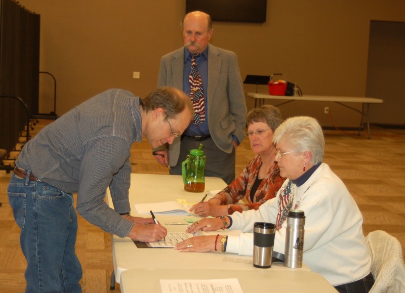 At Van Buren Precinct 3, Nathan Warstler signs in early this afternoon to vote. Morning and lunchtime voting was light but steady, Precinct Judge Allen Brunjes said.  From left are Warstler, Brunjes and poll workers Kay Tusing and Mary Duncan. (Photo by Jodi Magallanes)