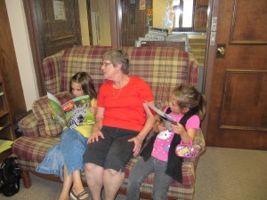 Every Wednesday children are invited to come in and read to a library volunteer for an extra prize from the display case. Pictured is one library volunteer, Judy Rowe, reading with Leah and Savannah Shelby.  (Photo provided)