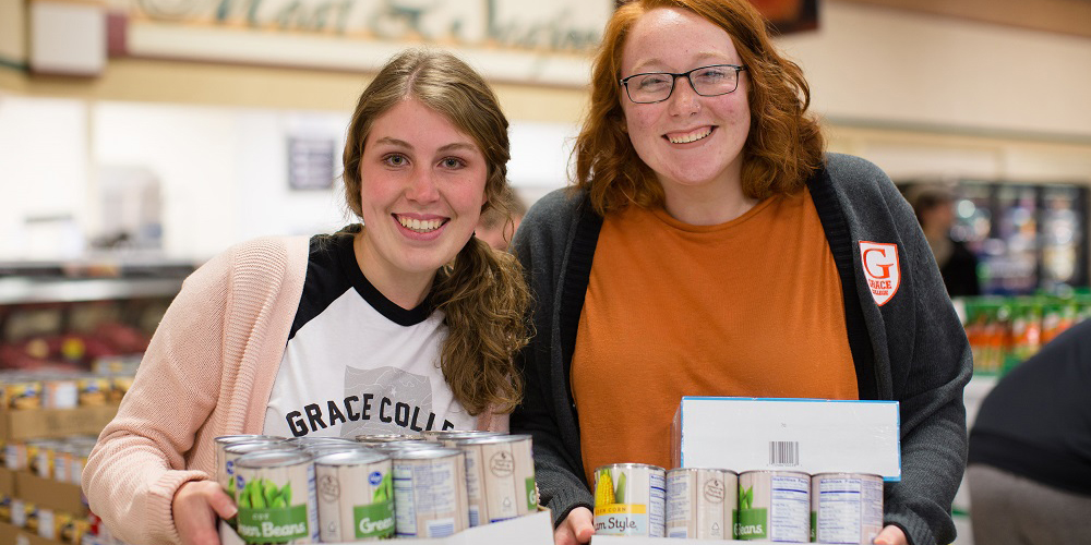 Grace College students Emily Roberts and Kendra Kooiker holding items for purchase at Supermarket Sweep.