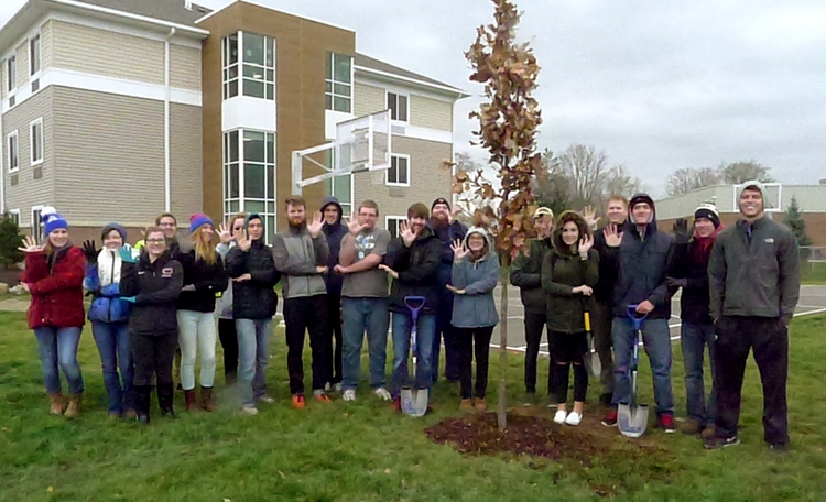 Grace College Environmental Ethics students, Dr. Nate Bosch, and NIPSCO Regional Project Manager Caryl Schwaller and Utility Arborist Chelsea Nepodal make the sign for “tree” as they stand behind the Swamp White Oak, which was planted by the recently constructed Omega Hall on campus. 